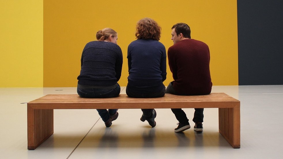 Drei Personen von hinten auf einer Bank in einem Museum sitzend