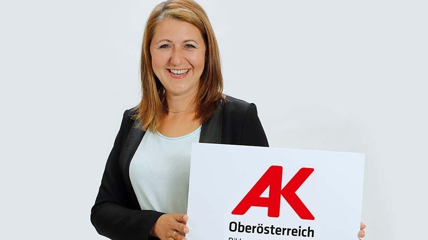 Eine Frau hält ein Schild hoch auf dem das Logo der Arbeiterkammer OÖ drauf ist.