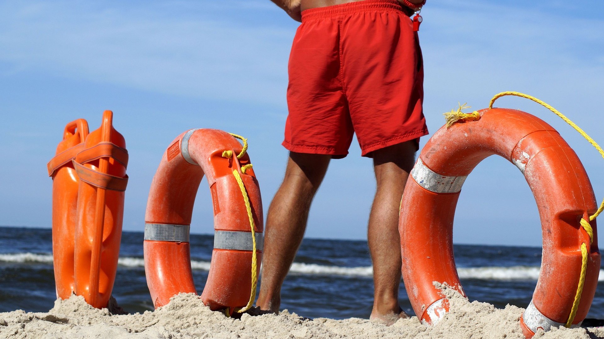 Am Meer steht ein Rettungsschwimmer mit Rettungsringen